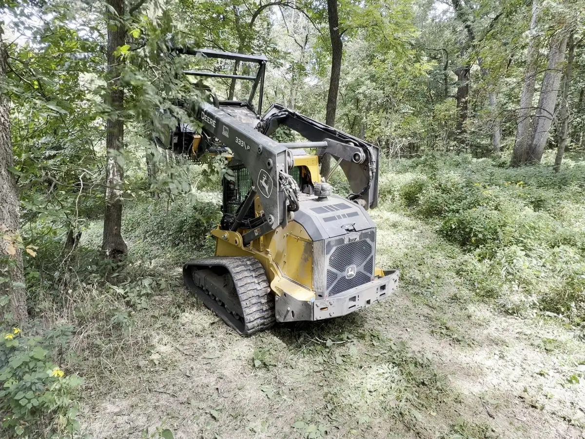 Mulching head cutting through branches, Deere cab visible behind