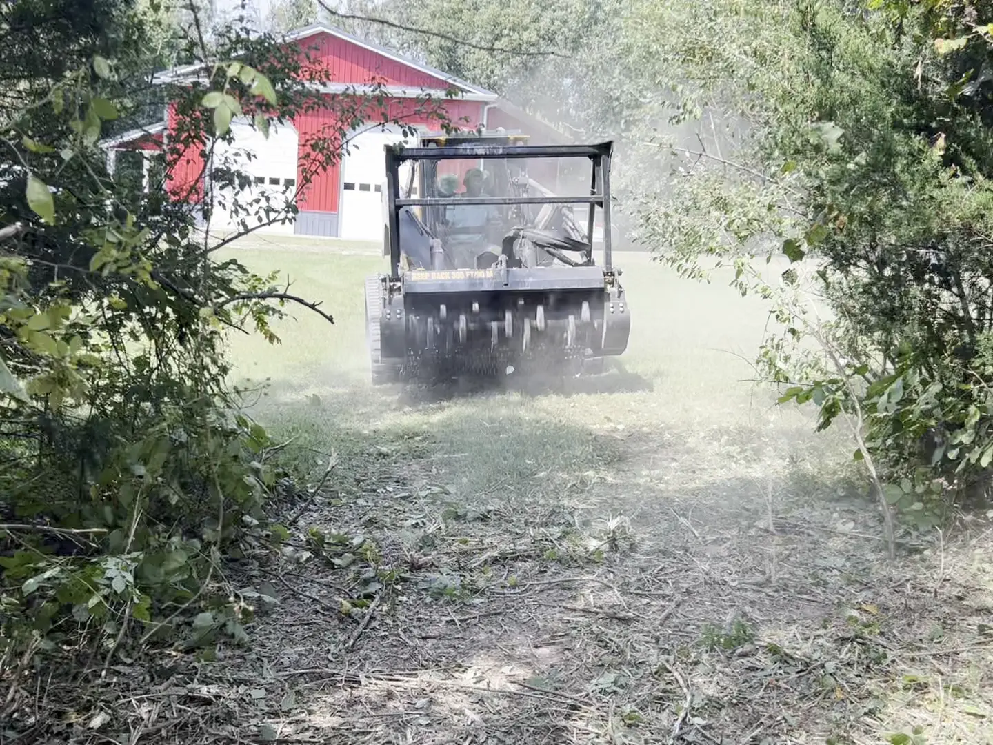 Mulcher clearing overgrown brush with a red barn visible behind