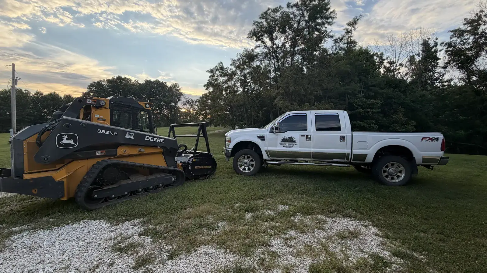 Company truck and forestry mulcher parked at sunset