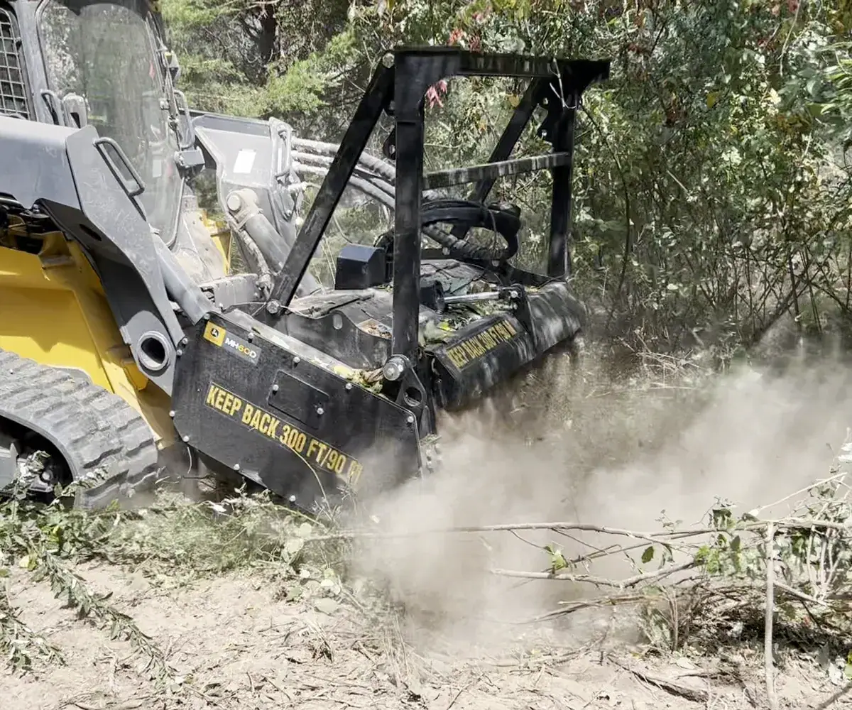 Forestry mulcher grinding brush with the head down in a cloud of dust